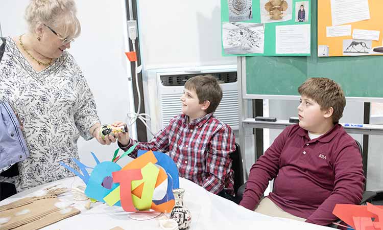 Teacher and 2 young male students discussing their art projects.