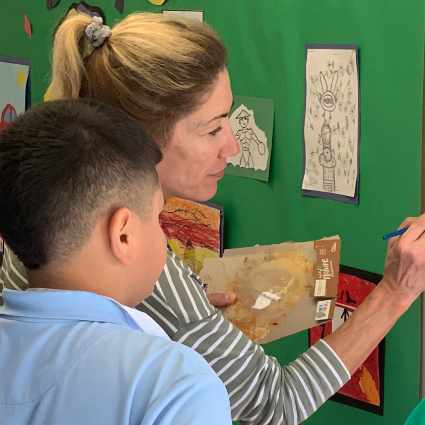 Female teacher painting a mural with a male student.