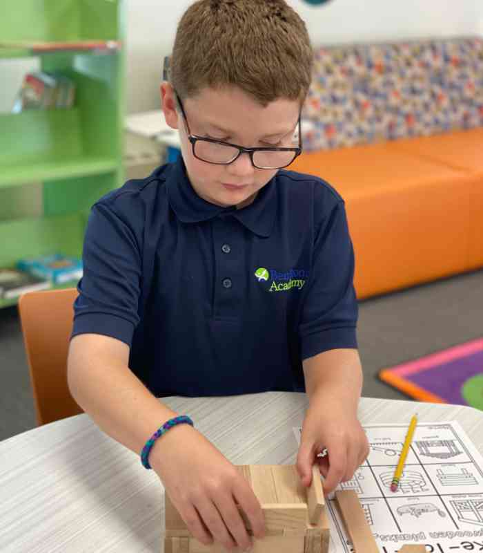 Young boy with glasses sitting at a table concentrating on putting a wooden puzzle together. Dyslexia