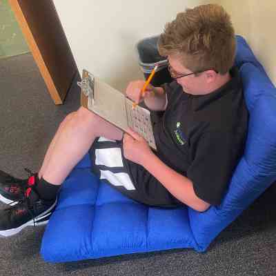 Young boy sitting in bean bag type chair holding a clip board.