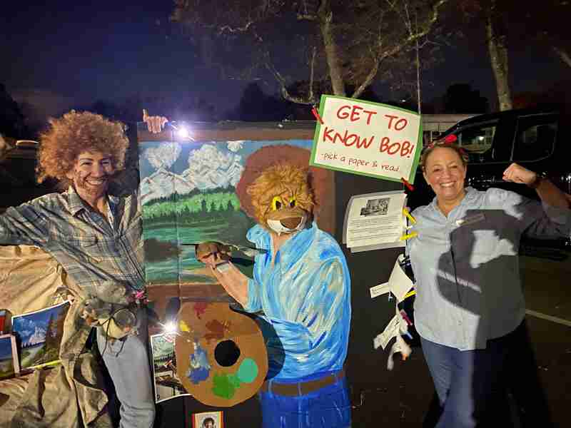 Person dressed up as artist Bob Ross holding a painting.