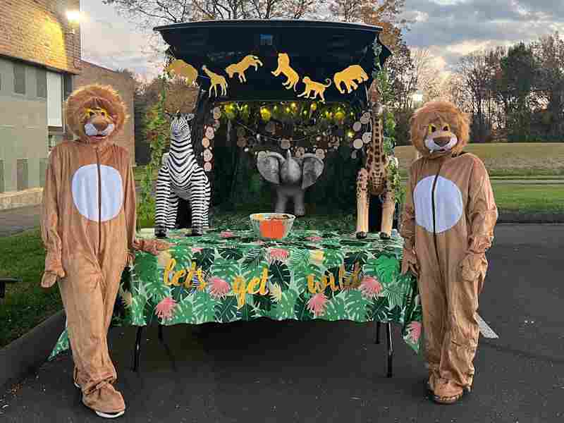 trunk or treat 2 - Ben Bronz Academy 2 people in lion Halloween costumes standing before bback of pickup truck decorated in Safari theme.