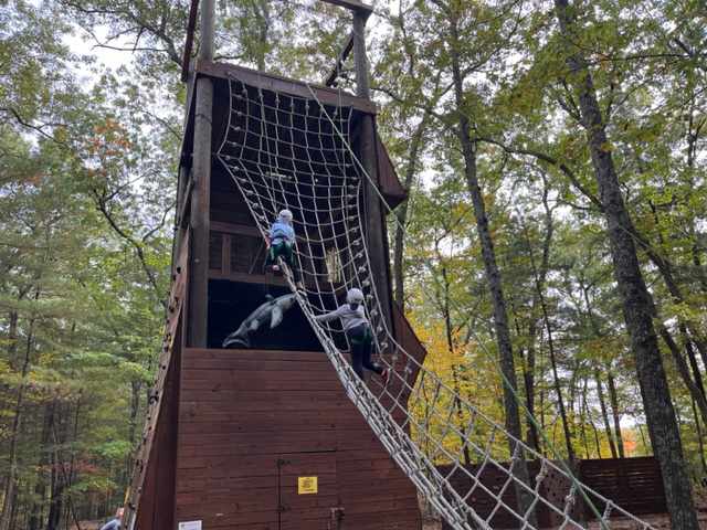 2 students making their way across the net to the wood platform on the obstacle course.