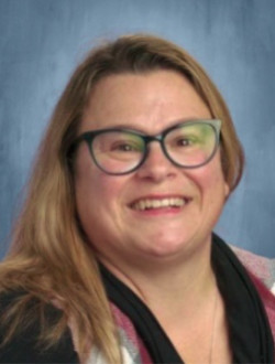 Smiling woman with long dark blond hair, wearing glasses.