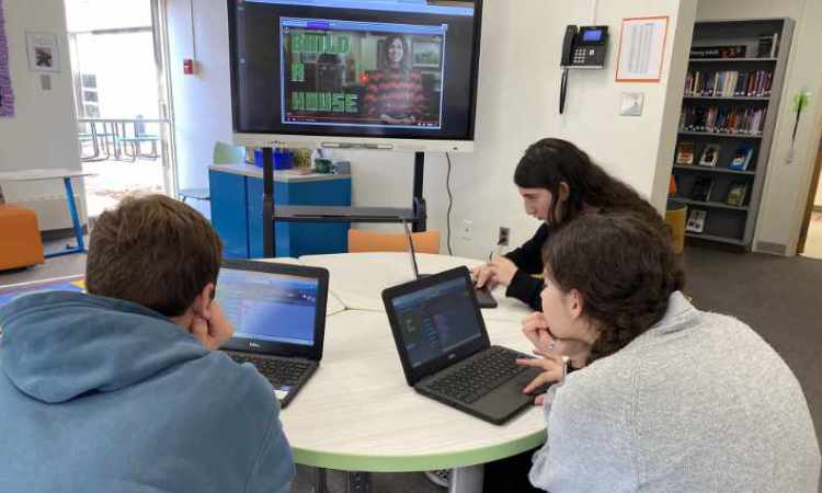 3 Students sitting at a round table working on their laptops.