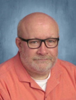 Male teacher with glasses, wearing an orange shirt.