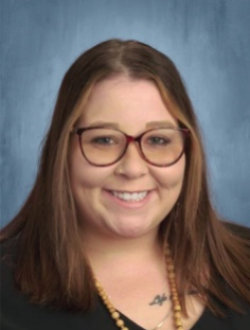 Young, smiling woman, with long brown hair, wearing glasses.