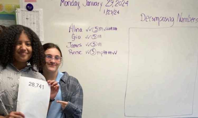 Two female students standing in front of white board.