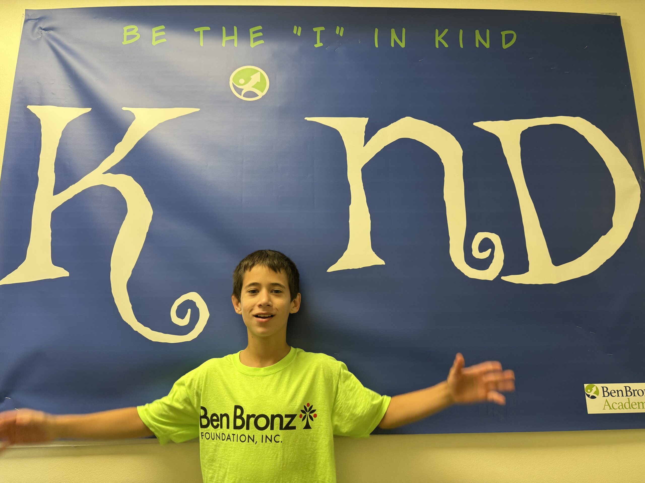 IMG_4925 Young male students spreading his arms in front of banner replacing the letter "I" in the word "Kind."